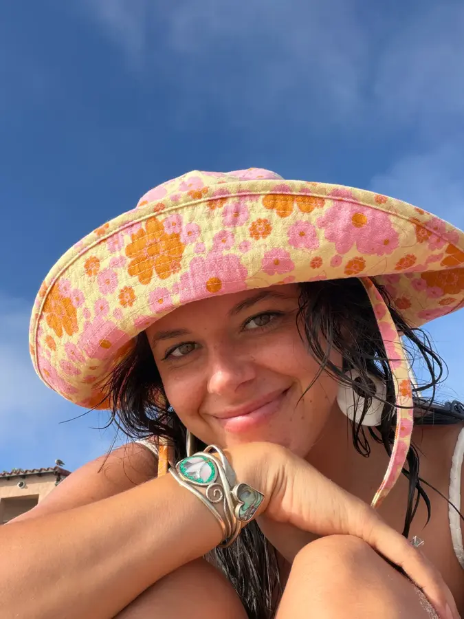Ali at the beach holding up a striped towel against a blue sky