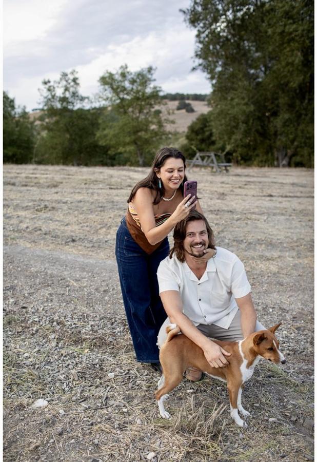 Ali filming on her phone while Sig crouches with a dog in a golden field