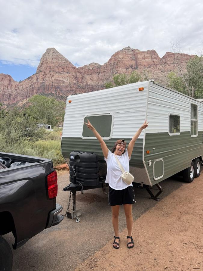 Ali throwing peace signs in front of the green trailer under Zion’s red cliffs