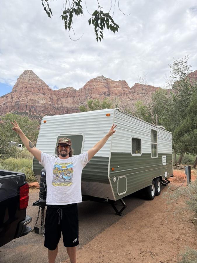 Sig throwing peace signs in front of the green trailer under Zion’s red cliffs